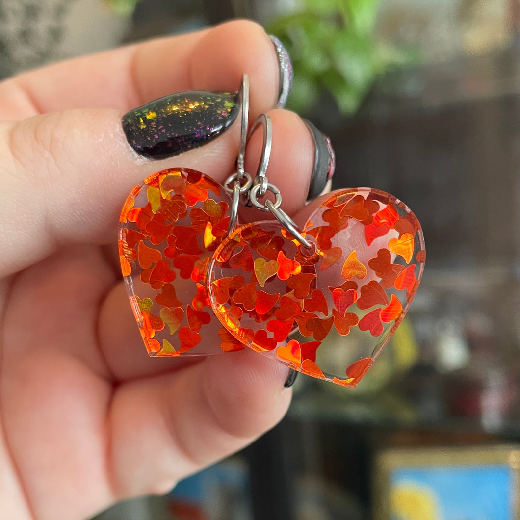 Petites boucles d'oreilles coeurs pendantes en acrylique transparente avec des confettis coeurs oranges holographiques