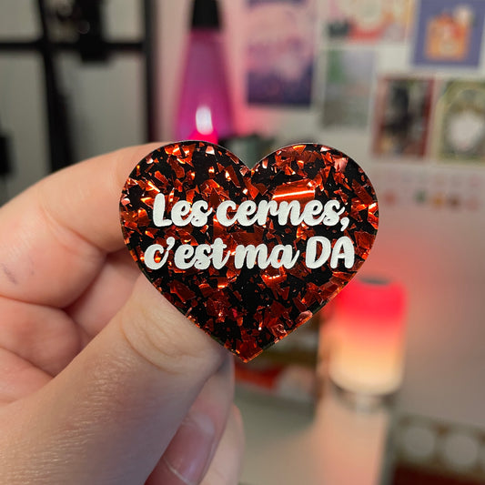 Broche "Les cernes, c'est ma DA" en acrylique noire avec des éclats de confettis rouges