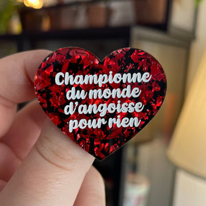 Broche "Championne du monde d'angoisse pour rien" en acrylique noire avec des éclats de confettis rouges
