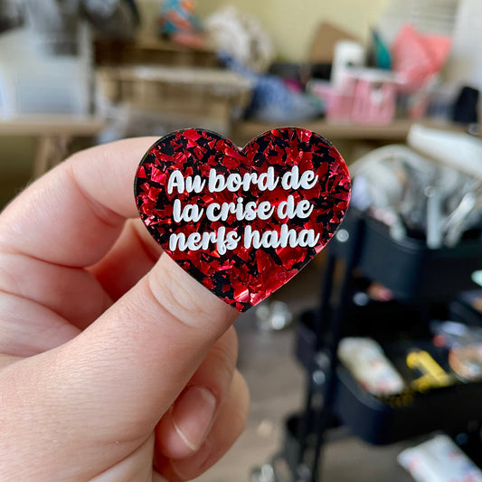 Broche "Au bord de la crise de nerfs haha" en acrylique noire avec des éclats de confettis rouges