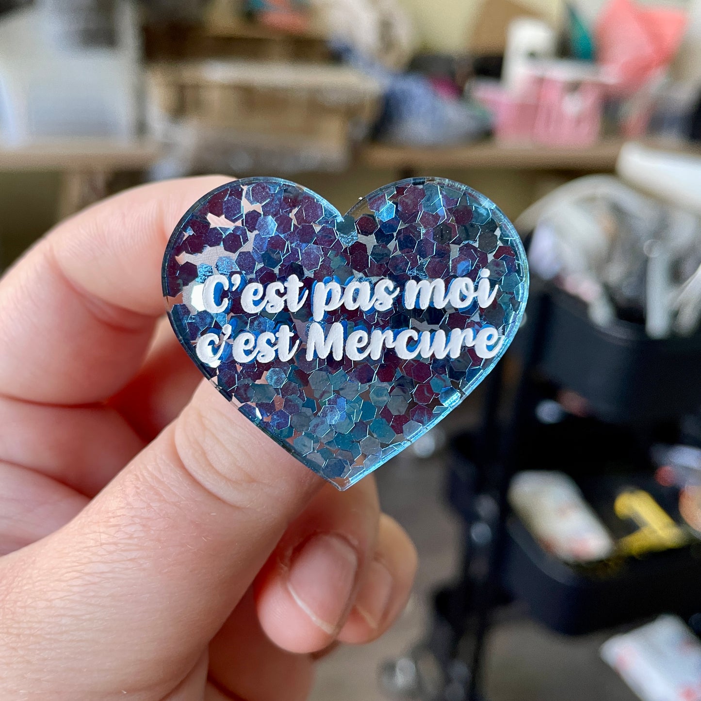 Broche "C'est pas moi c'est Mercure" en acrylique semi-transparente avec des confettis bleus