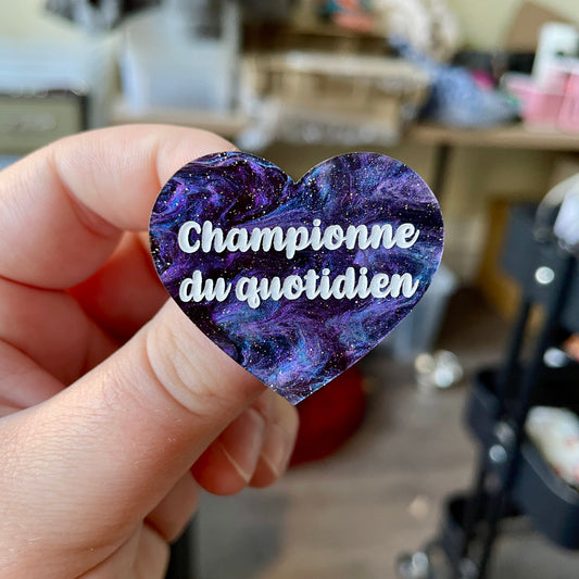 Broche "Championne du quotidien" en acrylique marbrée noire, bleue et violette à paillettes