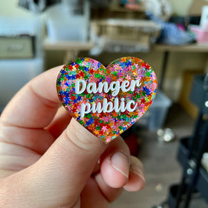 Broche "Danger public" en acrylique semi-transparente avec des confettis étoiles multicolores