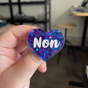 [CONTRÔLE TECHNIQUE] Broche "Non" en acrylique transparente avec des éclats de confettis bleus et roses/violets