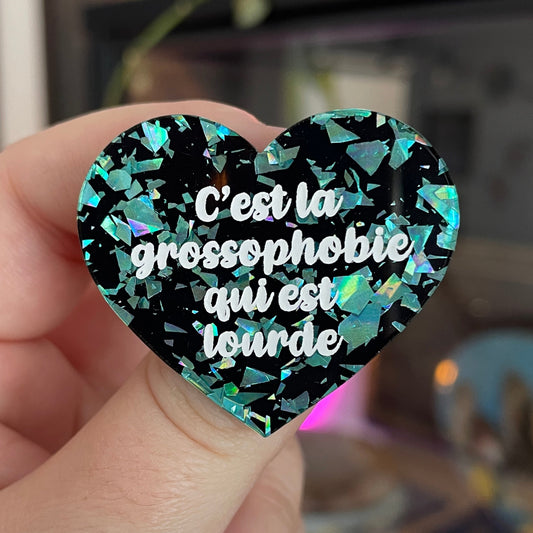 Broche "C'est la grossophobie qui est lourde" en acrylique noire avec des éclats de confettis turquoise