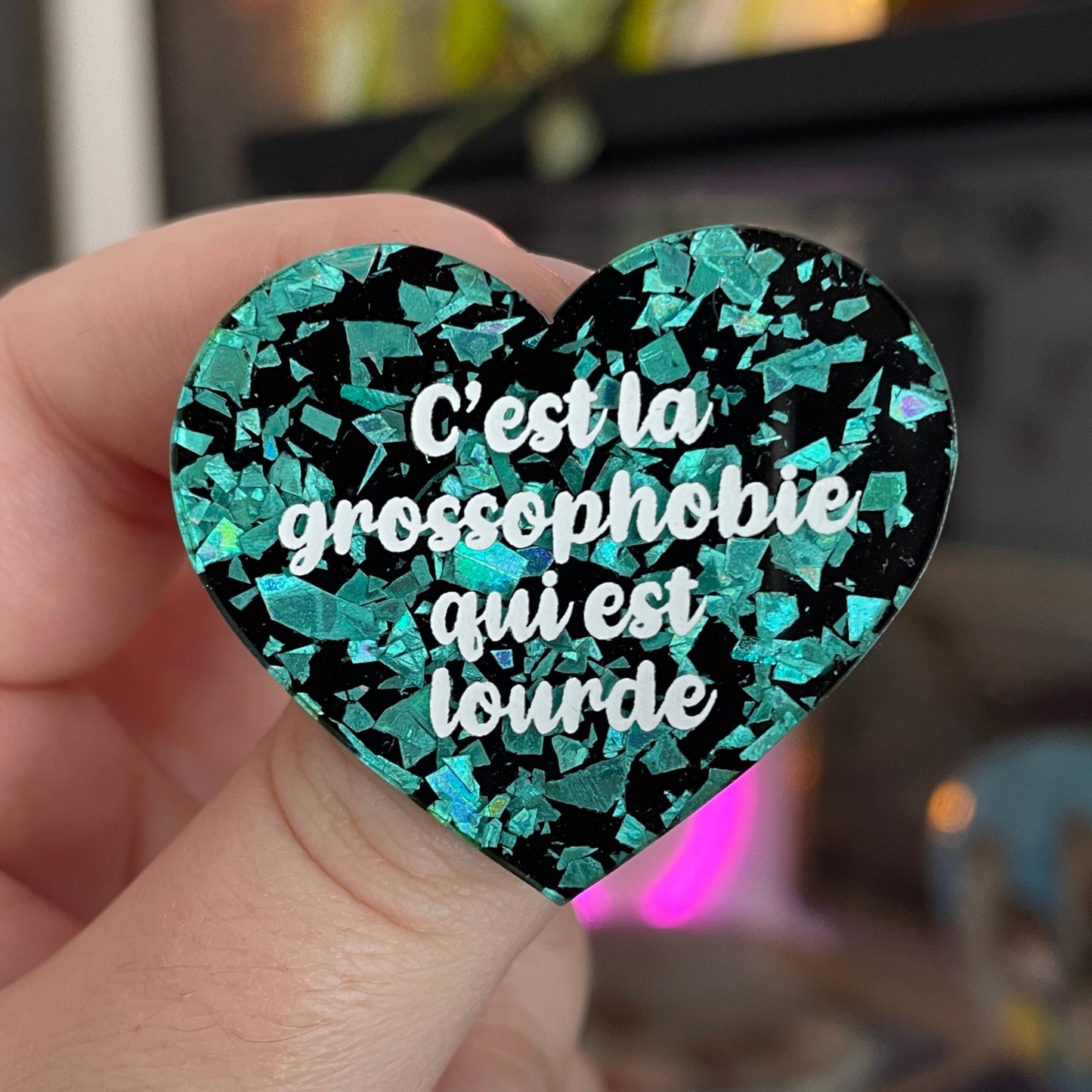 Broche "C'est la grossophobie qui est lourde" en acrylique noire avec des éclats de confettis turquoise