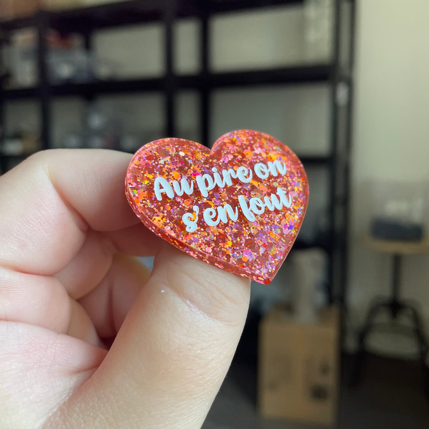 Broche "Au pire on s'en fout" en acrylique semi transparente avec des paillettes corail