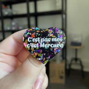 Broche "C'est pas moi c'est Mercure" en acrylique noire avec des éclats de confettis multicolores