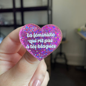 Broche "La féministe qui rit pas à tes blagues" en acrylique semi transparente avec des paillettes violettes