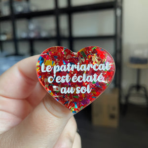 Broche "Le patriarcat c'est éclaté au sol" en acrylique transparente avec des éclats de confettis rouges et multicolores