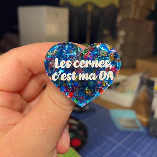 [Contrôle technique] Broche "Les cernes c'est ma DA" en acrylique transparente avec des confettis bleus et multicolores