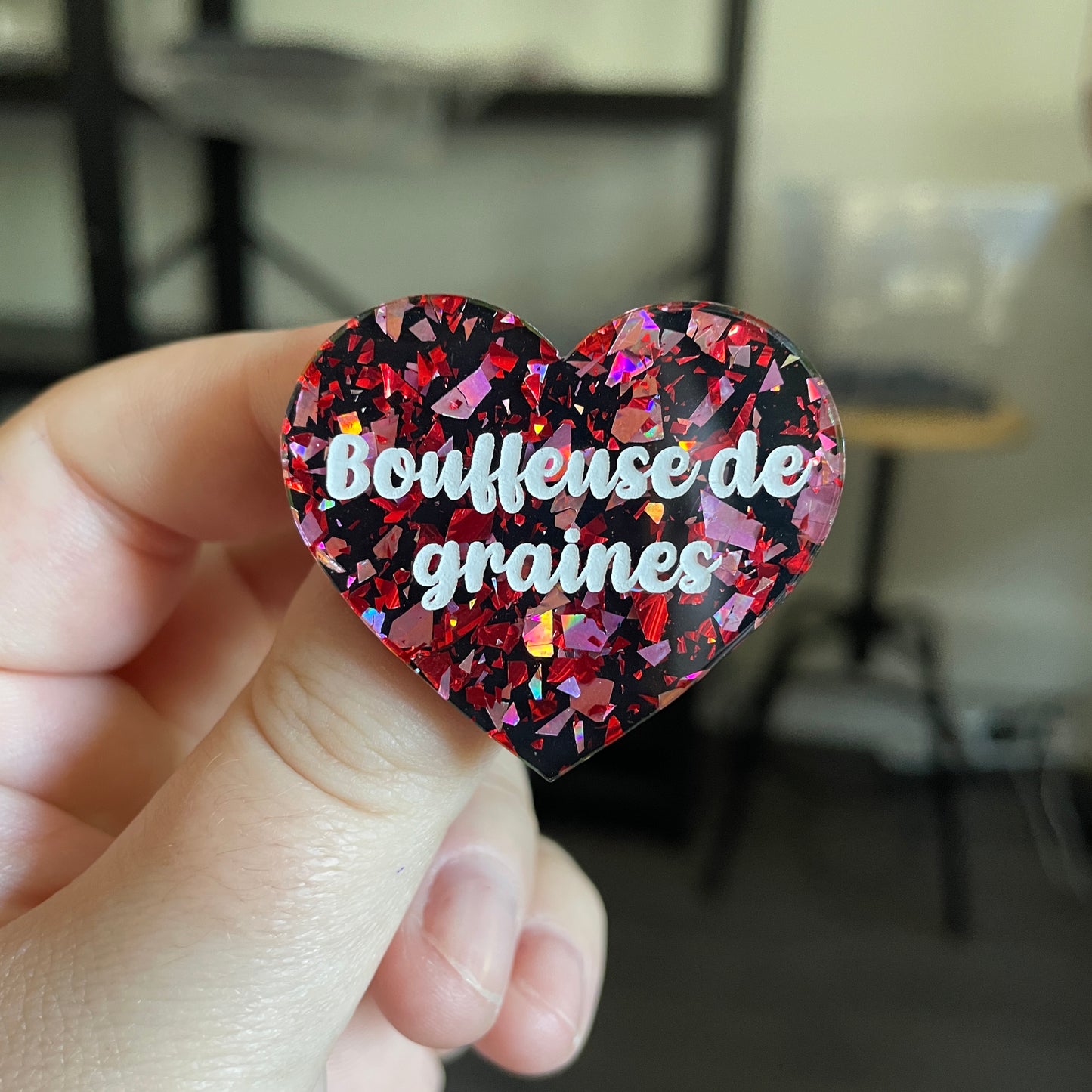 Broche "Bouffeuse de graines" en acrylique noire avec des éclats de confettis rouges et roses