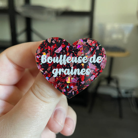 Broche "Bouffeuse de graines" en acrylique noire avec des éclats de confettis rouges et roses