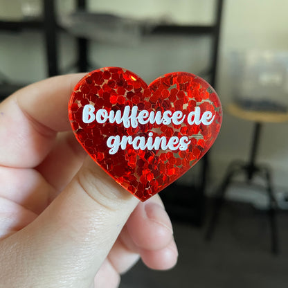 Broche "Bouffeuse de graines" en acrylique semi transparente avec des confettis rouges