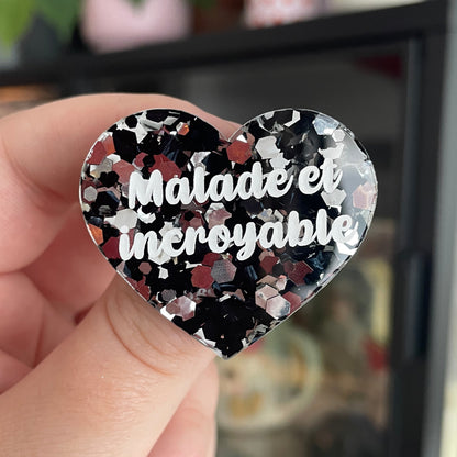 Broche "Malade et incroyable" en acrylique semi transparente avec des confettis noirs et argentés