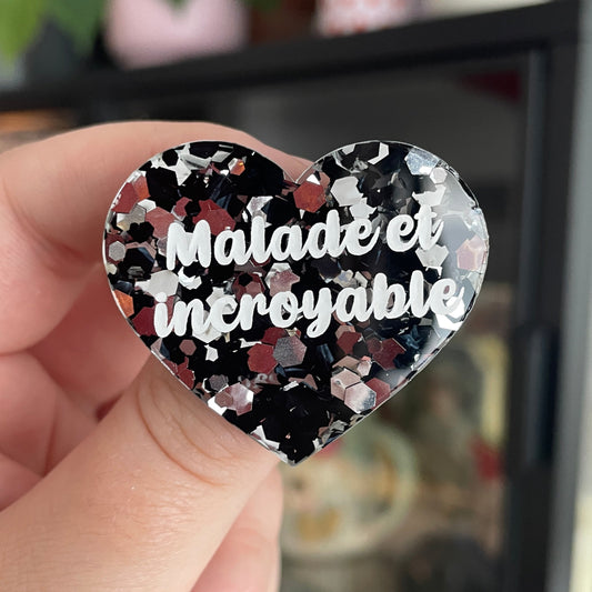Broche "Malade et incroyable" en acrylique semi transparente avec des confettis noirs et argentés