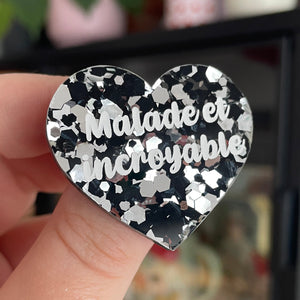 Broche "Malade et incroyable" en acrylique semi transparente avec des confettis noirs et argentés