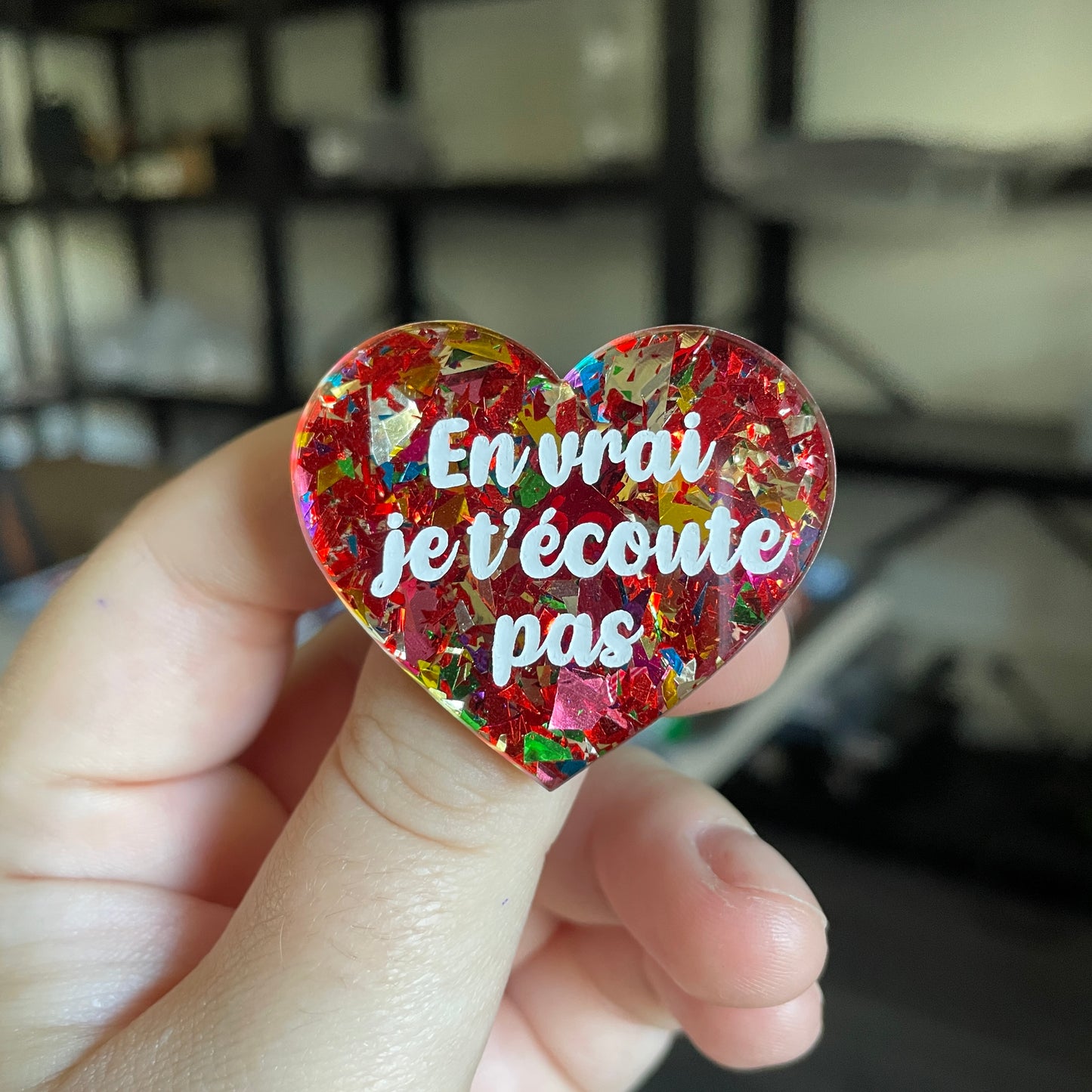 Broche "En vrai je t'écoute pas" en acrylique transparente avec des éclats de confettis rouges et multicolores