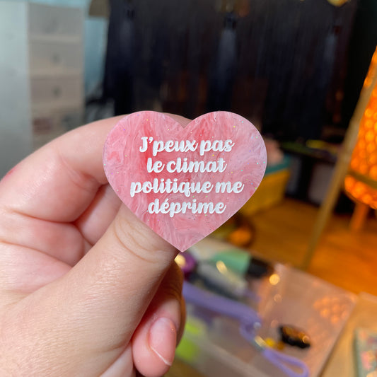 Broche "J'peux pas le climat politique me déprime" en acrylique semi transparente marbrée rose et blanche à paillettes