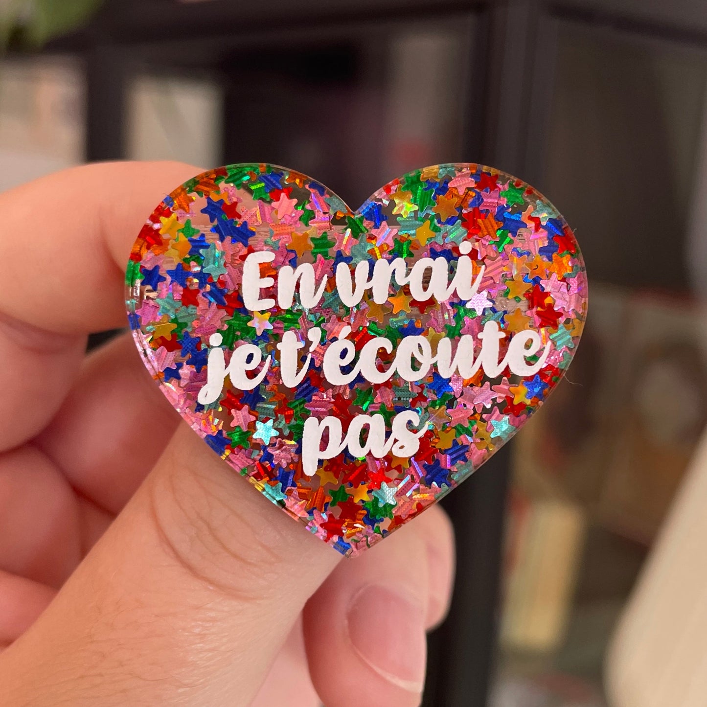 Broche "En vrai je t'écoute pas" en acrylique semi-transparente avec des confettis étoiles multicolores