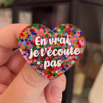 Broche "En vrai je t'écoute pas" en acrylique semi-transparente avec des confettis étoiles multicolores