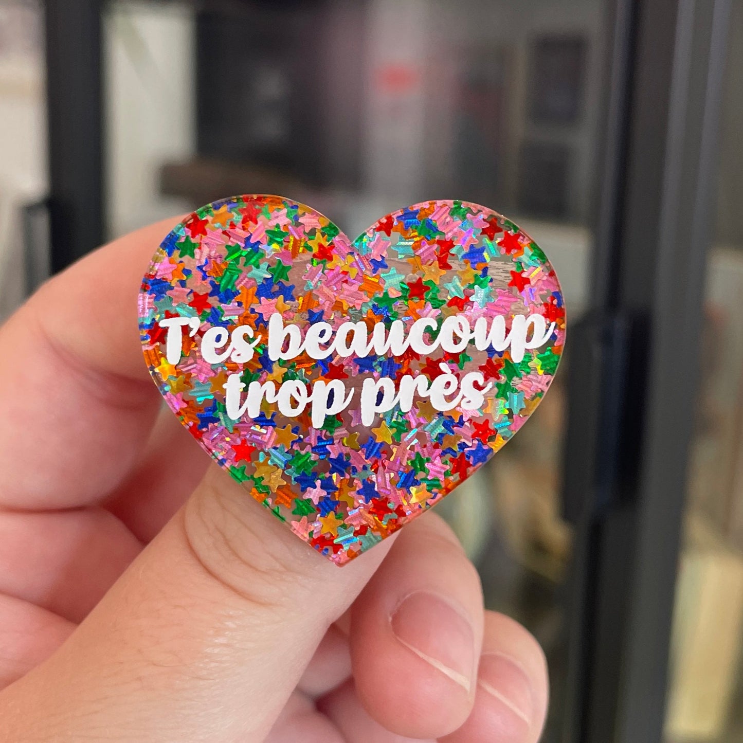 Broche "T'es beaucoup trop près" en acrylique semi-transparente avec des confettis étoiles multicolores