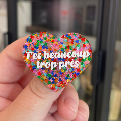 Broche "T'es beaucoup trop près" en acrylique semi-transparente avec des confettis étoiles multicolores