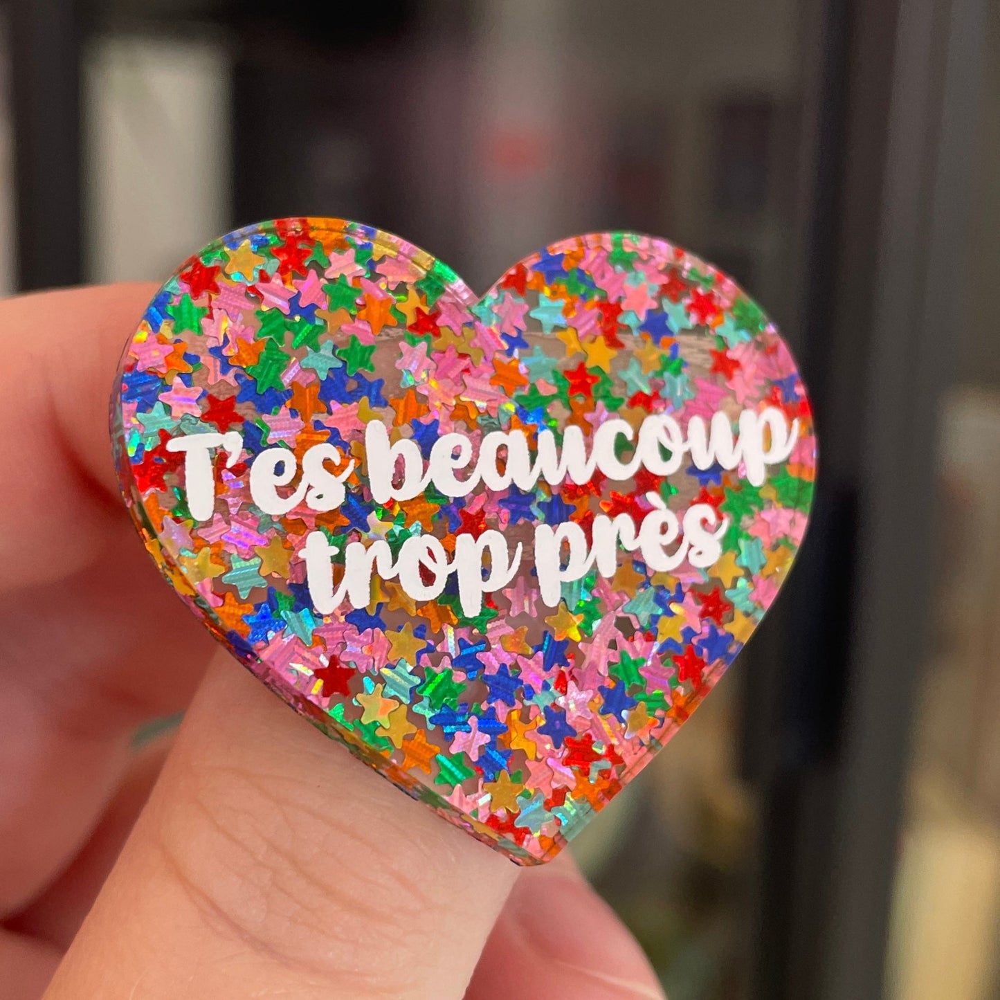 Broche "T'es beaucoup trop près" en acrylique semi-transparente avec des confettis étoiles multicolores