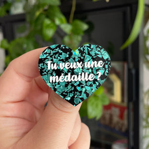 Broche "Tu veux une médaille ?" en acrylique noire à confettis galactiques turquoise