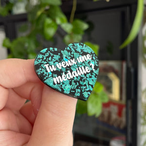 Broche "Tu veux une médaille ?" en acrylique noire à confettis galactiques turquoise