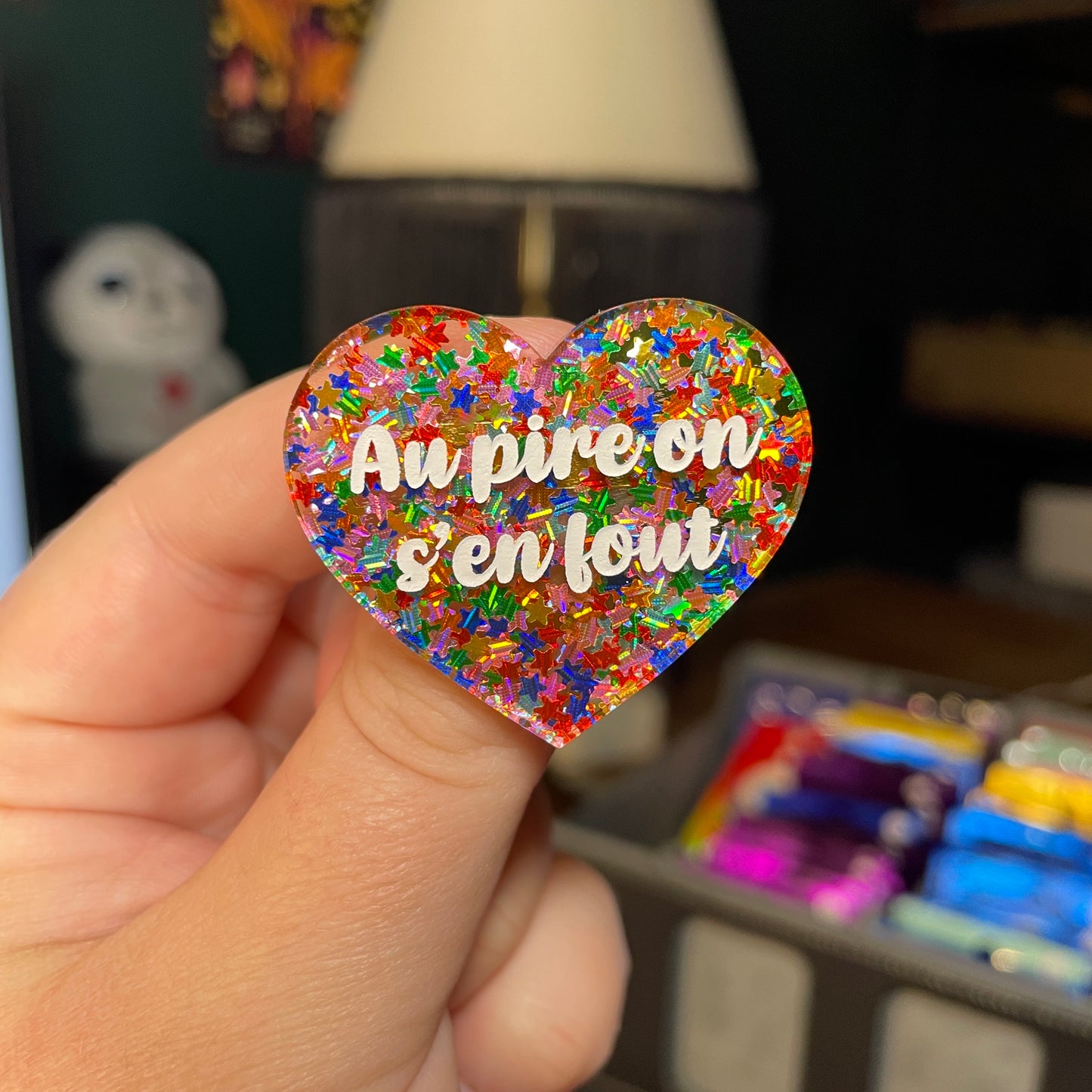 Broche "Au pire on s'en fout" en acrylique semi transparente avec des étoiles multicolores