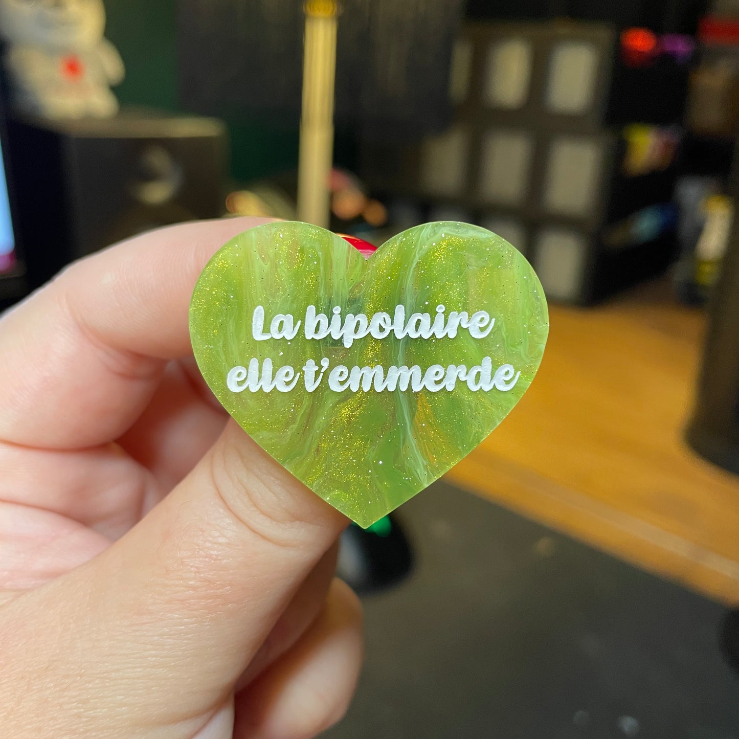 [Contrôle technique] Broche "La bipolaire elle t'emmerde" en acrylique semi transparente marbrée verte et dorée à paillettes