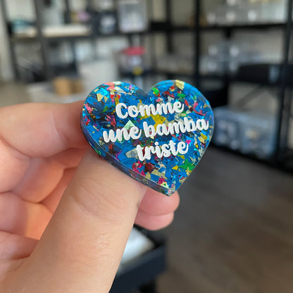 [CONTRÔLE TECHNIQUE] Broche "Comme une bamba triste" en acrylique transparente avec des éclats de confettis bleus et multicolores