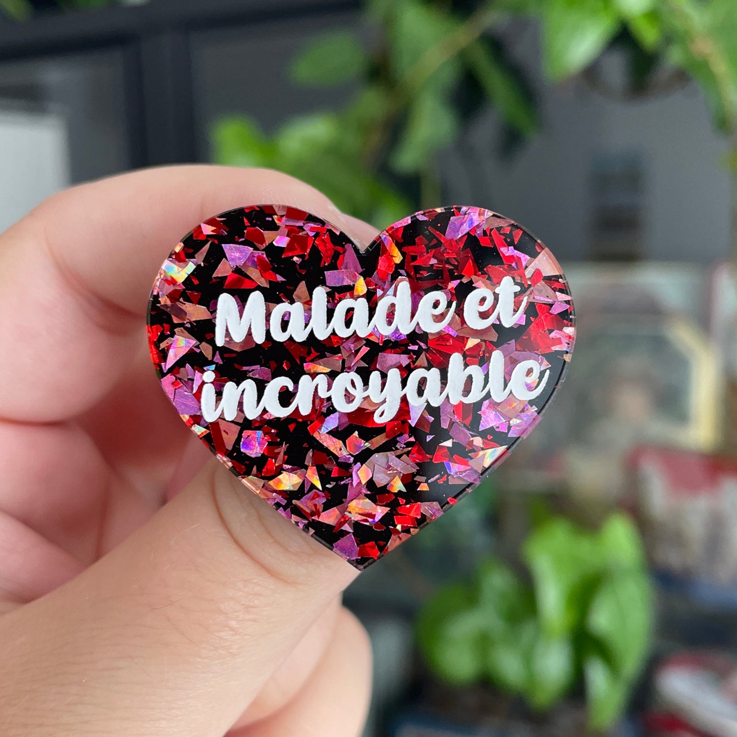 Broche "Malade et incroyable" en acrylique noire avec des éclats de confettis rouges et roses