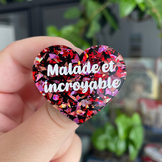 Broche "Malade et incroyable" en acrylique noire avec des éclats de confettis rouges et roses