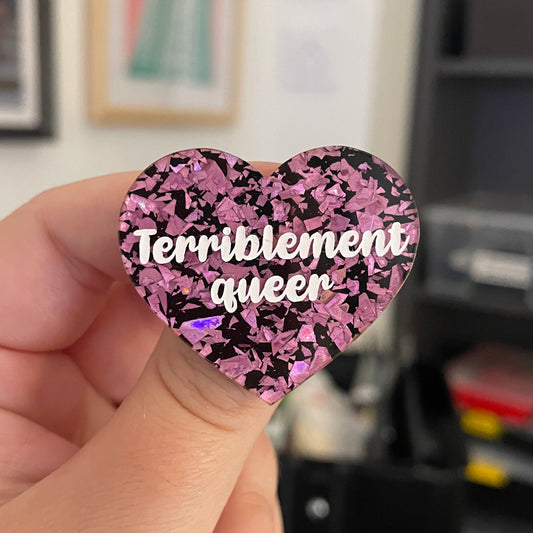[CONTRÔLE TECHNIQUE] Broche "Terriblement queer" en acrylique noire avec des éclats de confettis roses