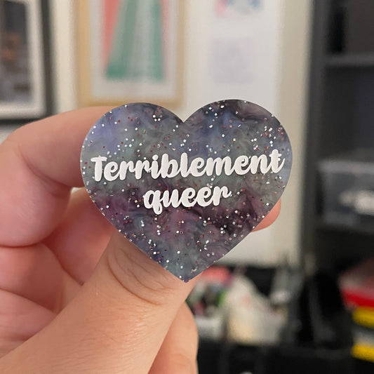 [CONTRÔLE TECHNIQUE] Broche "Terriblement queer" en acrylique marbrée grise, rose, noire et verte à paillettes