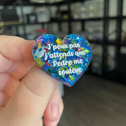 Broche "J'peux pas j'attends que Pedro me soulève" en acrylique transparente avec des éclats de confettis bleus et multicolores