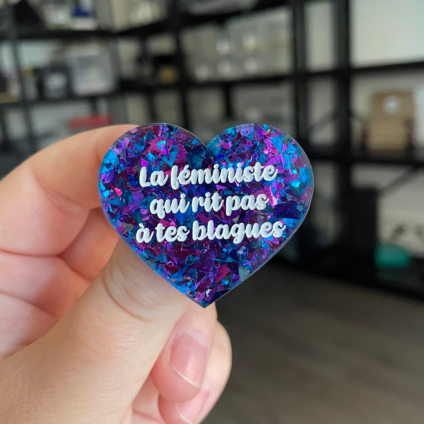 Broche "La féministe qui rit pas à tes blagues" en acrylique transparente avec des éclats de confettis bleus et violets