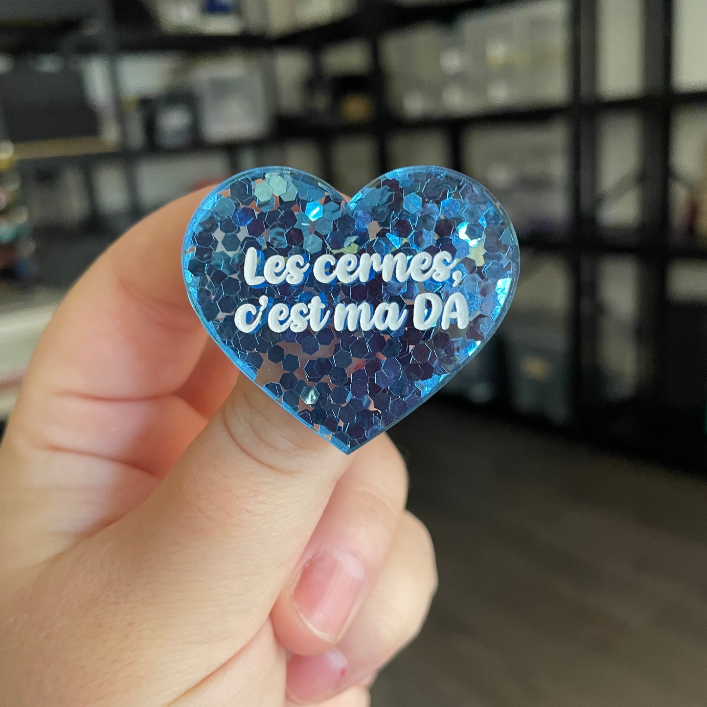 Broche "Les cernes, c'est ma DA" en acrylique semi transparente avec des confettis bleus