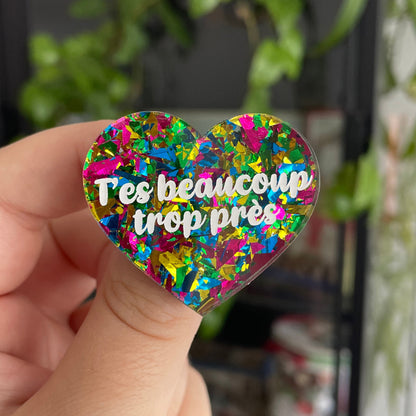 Broche "T'es beaucoup trop près" en acrylique transparente avec des éclats de confettis jaunes, verts, bleus et roses
