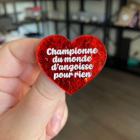 Broche "Championne du monde d'angoisse pour rien" en acrylique semi transparente avec des confettis rouges