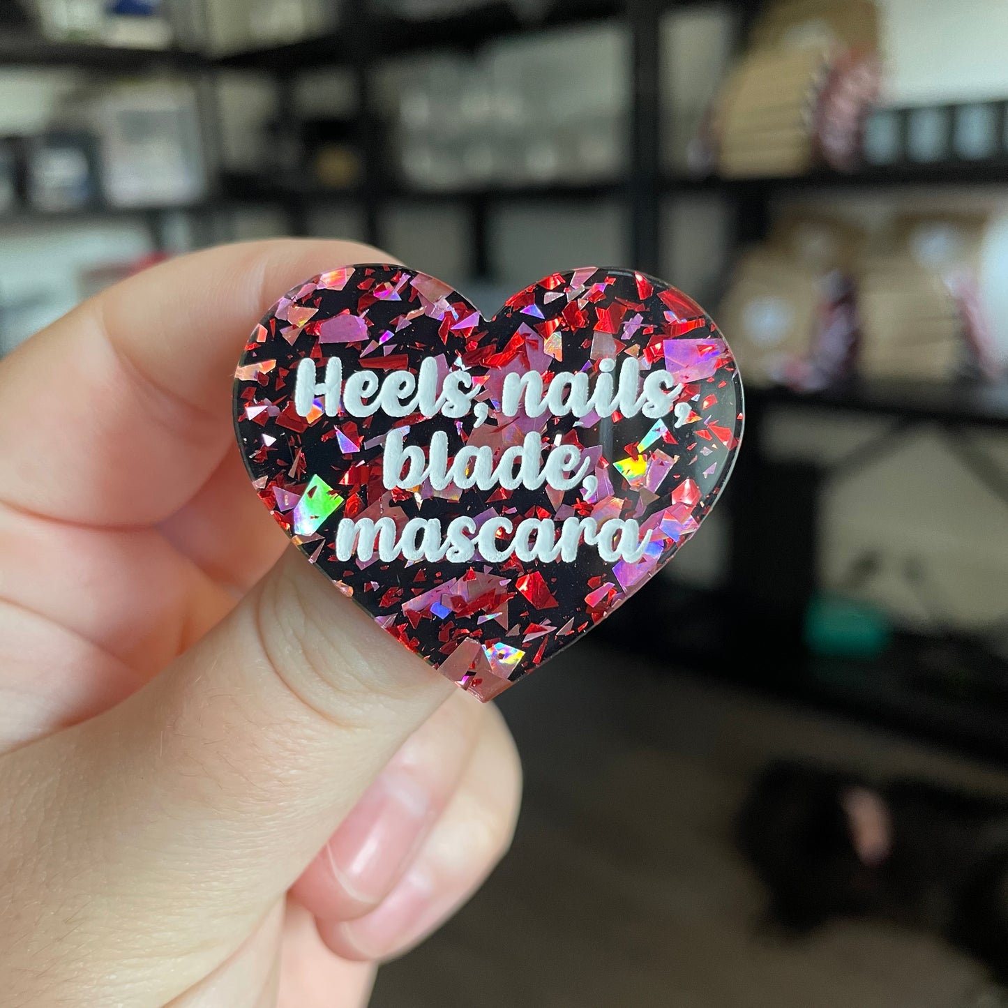 Broche "Heels, nails, blade, mascara" en acrylique noire avec des éclats de confettis rouges et roses
