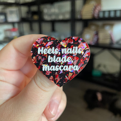 Broche "Heels, nails, blade, mascara" en acrylique noire avec des éclats de confettis rouges et roses