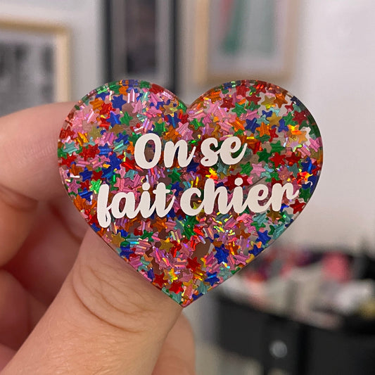 Broche "On se fait chier" en acrylique semi-transparente avec des confettis étoiles multicolores