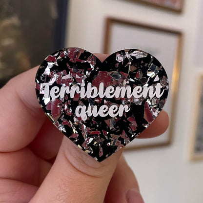 [CONTRÔLE TECHNIQUE] Broche "Terriblement queer" en acrylique noire avec des confettis argentés