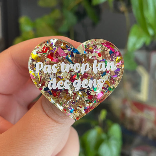 Broche "Pas trop fan des gens" en acrylique transparente avec des éclats de confettis dorés et multicolores