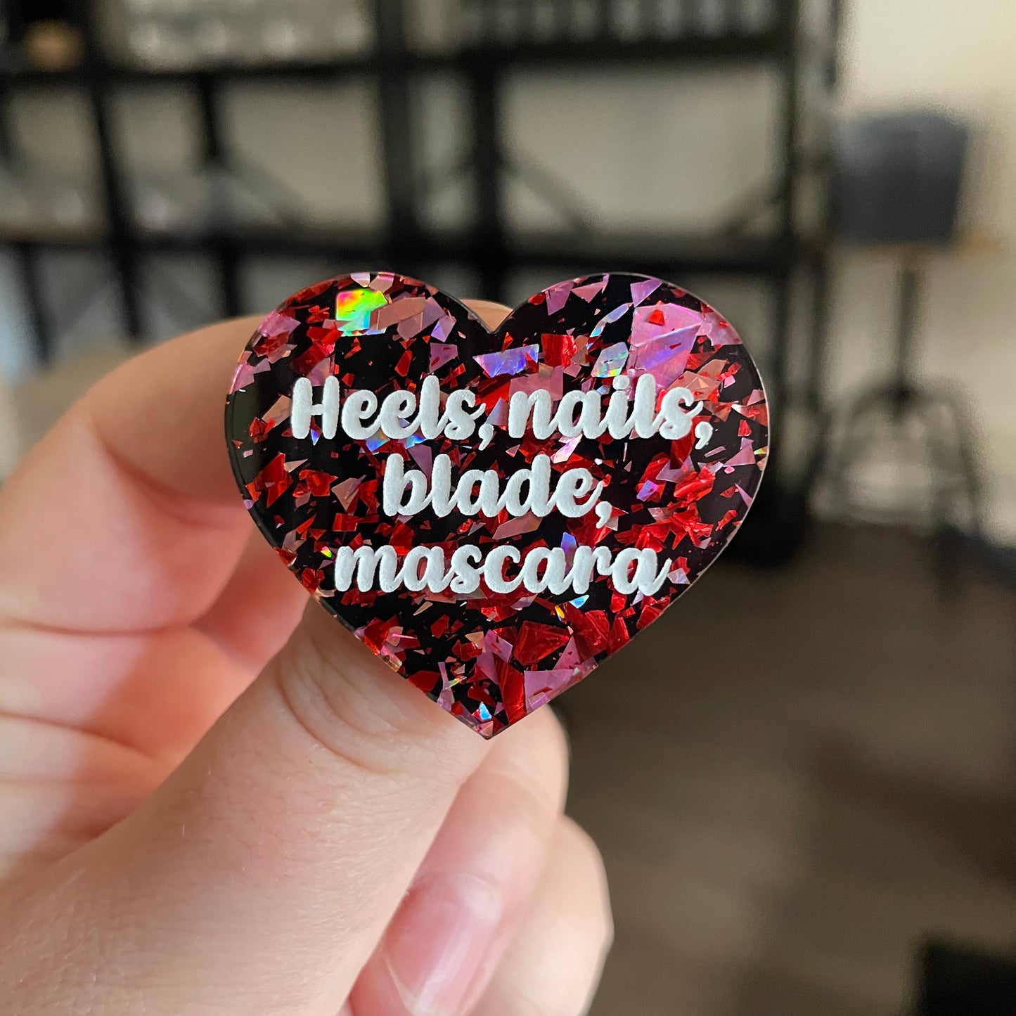 Broche "Heels, nails, blade, mascara" en acrylique noire avec des éclats de confettis rouges et roses