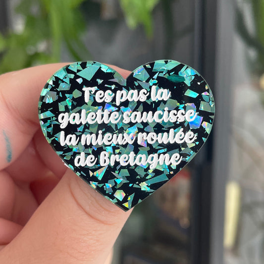 Broche "T'es pas la galette saucisse la mieux roulée de Bretagne" en acrylique noire avec des éclats de confettis turquoise