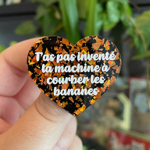 Broche "T'as pas inventé la machine à courber les bananes" en acrylique noire avec des éclats de confettis oranges